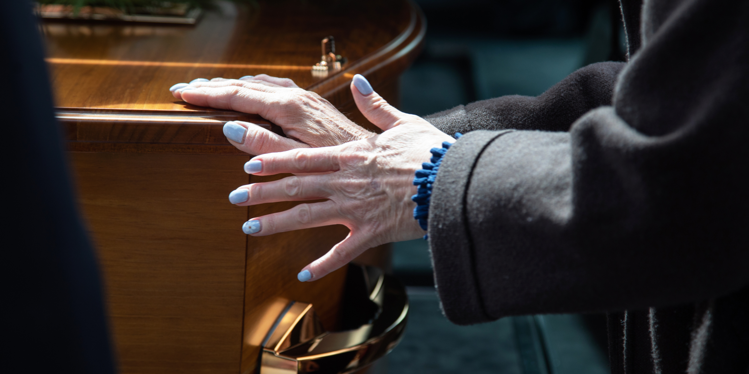 A woman's hands rest on a wooden casket.